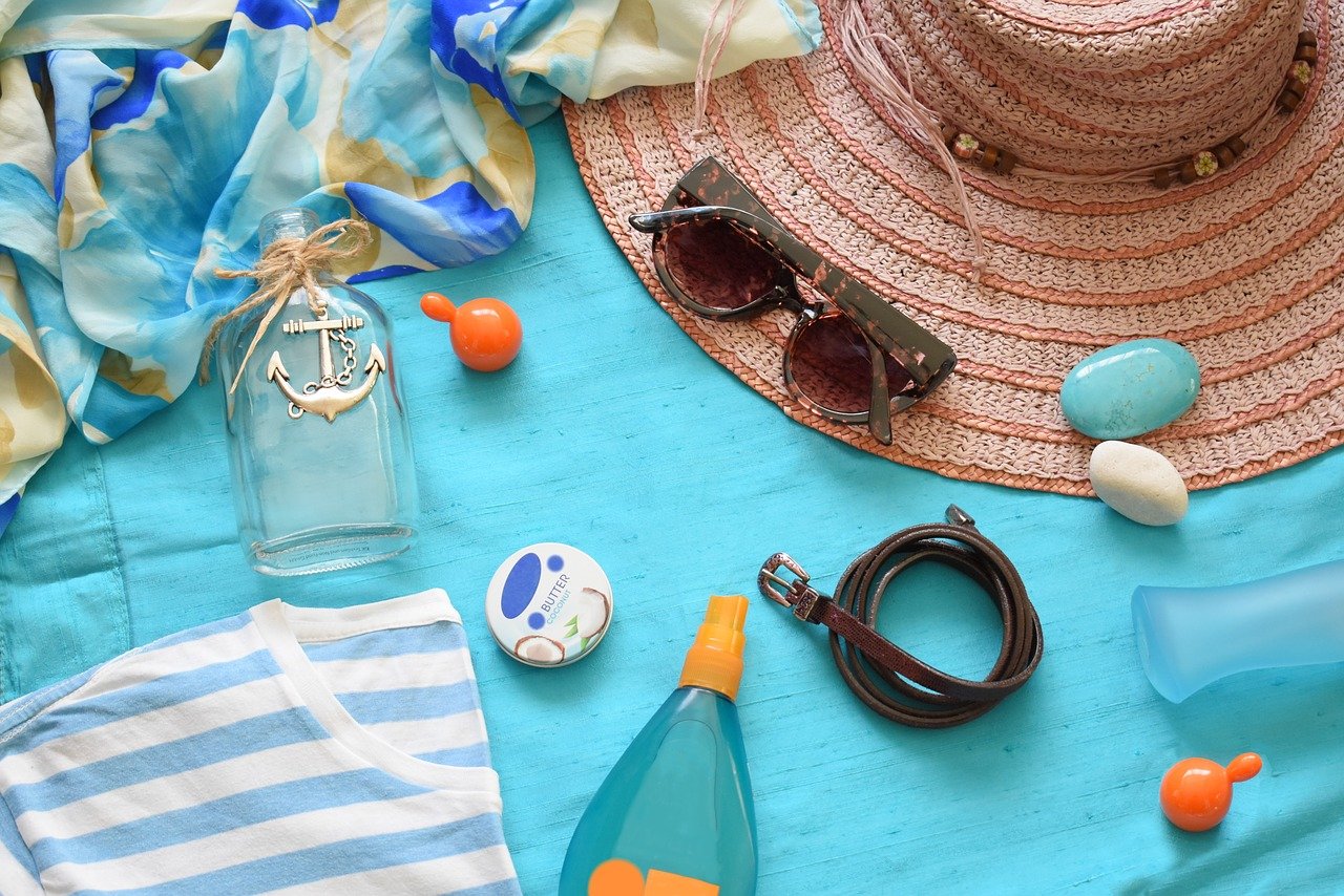 Óculos de sol, pedras coloridas, tecidos, cosméticos e chapéu sobre canga azul de praia