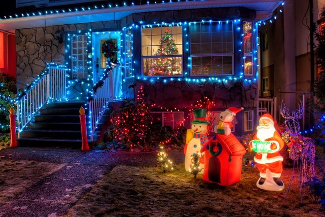 Fachada de casa decorada com luzes coloridas e estátuas natalinas.