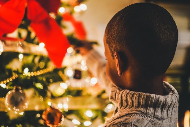 Menino pequeno olhando para árvore de Natal acesa.