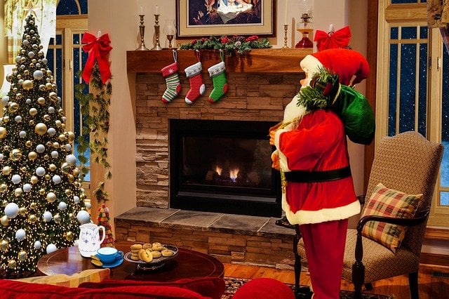 Sala com decoração natalina, estátua de Papai Noel e meias penduradas em cima de uma lareira.