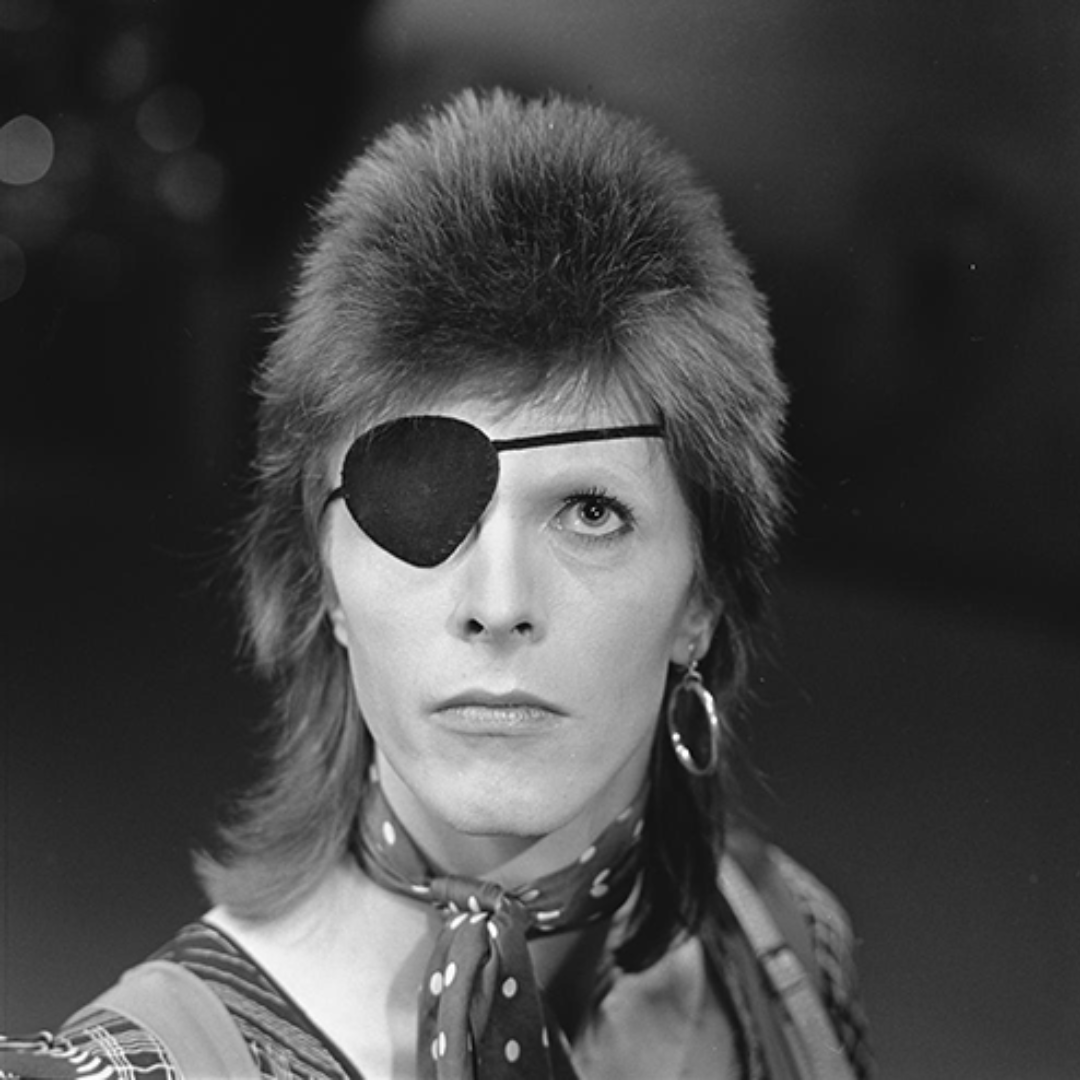 Foto de Bowie preto e branca. Ele usa brinco de argolas e um tapa-olho.