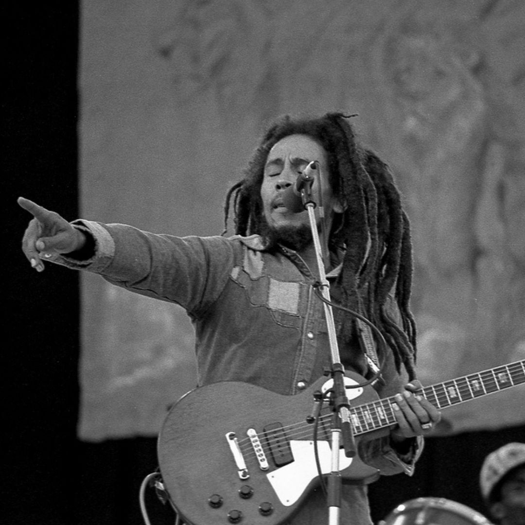 Imagem em preto e branco do cantor Bob Marley cantando e tocando em um show
