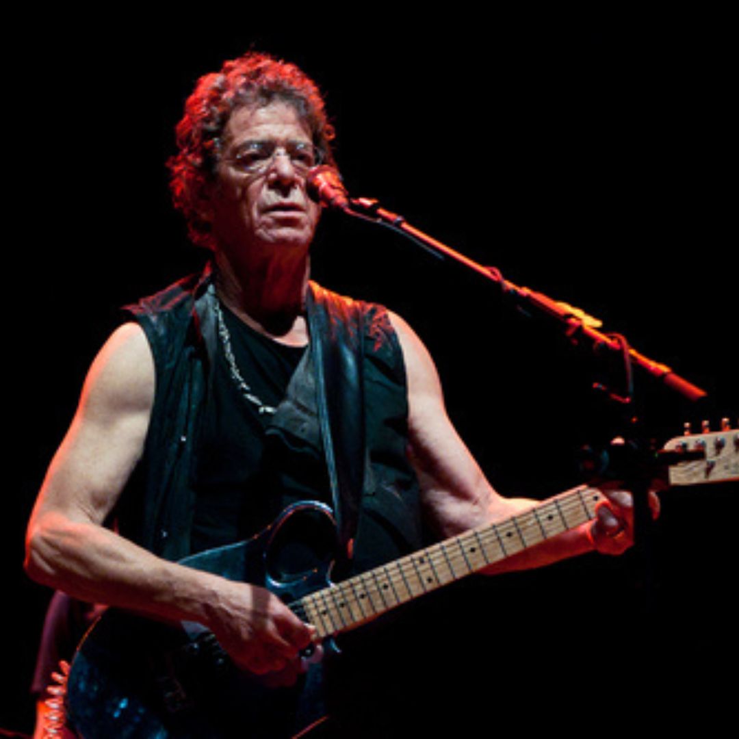Imagem do cantor Lou Reed tocando guitarra e cantando em um show