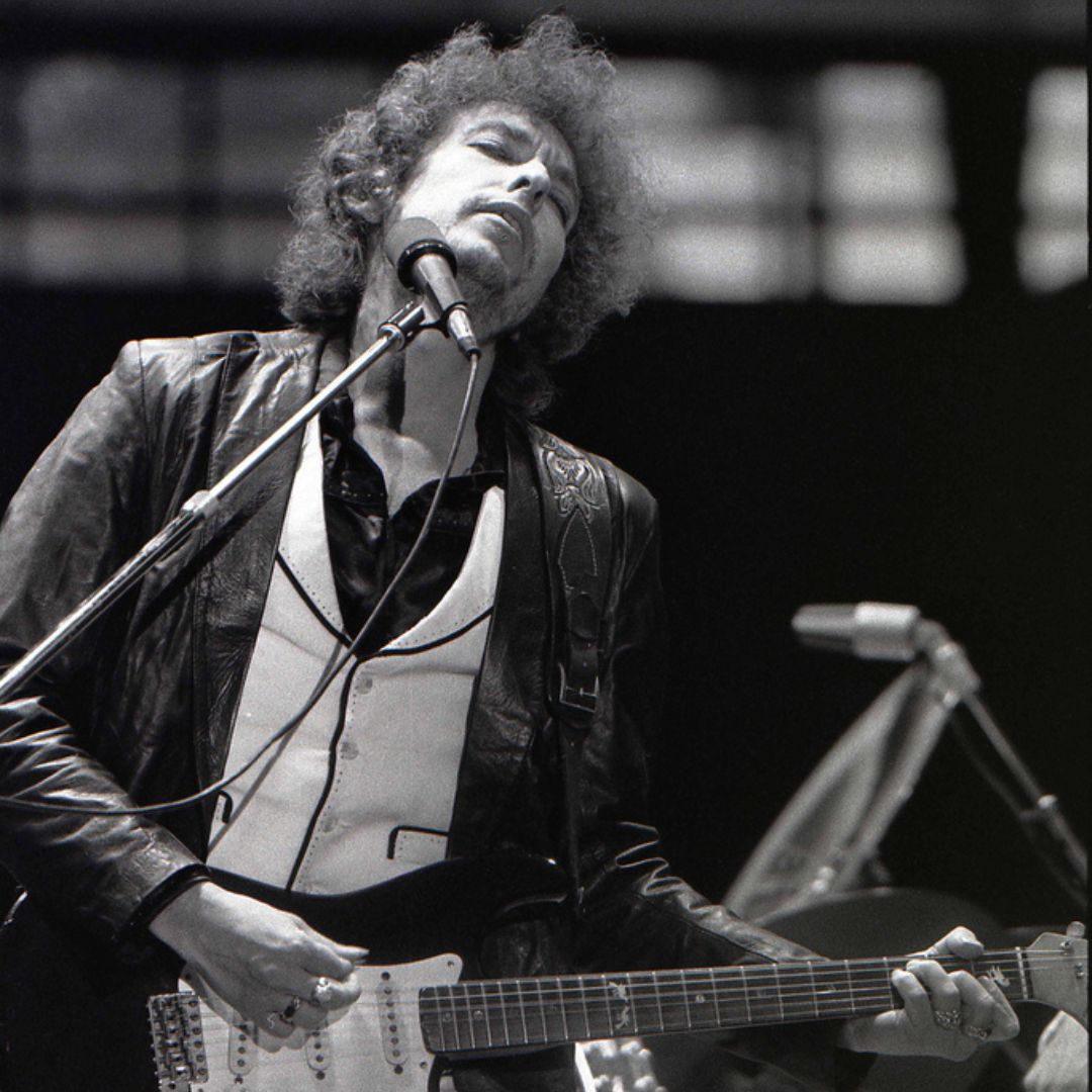 Imagem em preto e branco do cantor Bob Dylan tocando guitarra em um show