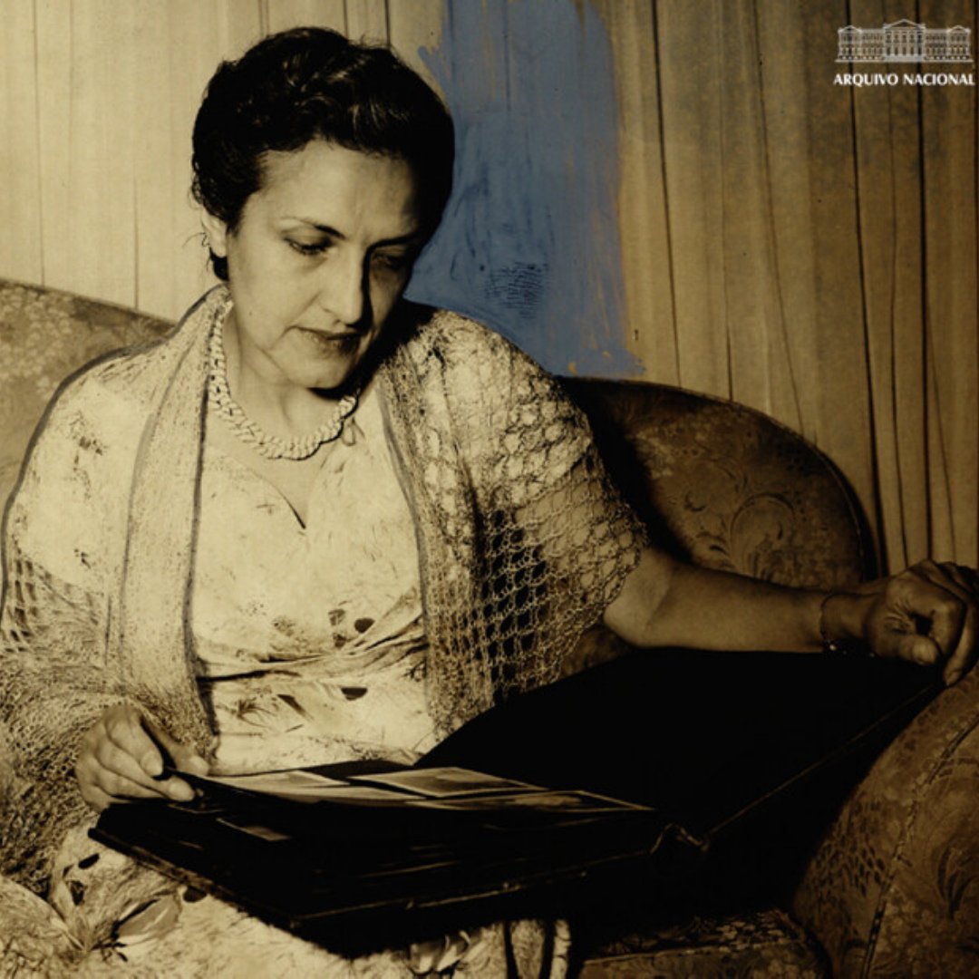 Imagem da poetisa Cecília Meireles sentada em um sofá, olhando um álbum de fotos