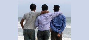 Três amigos abraçados lado a lado na praia.