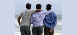 Mensagens Com Amor Três amigos abraçados lado a lado na praia.