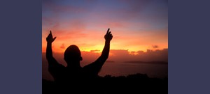 Homem com as mãos levantadas ao pôr do sol.