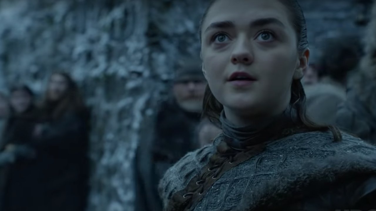 Reprodução/HBO Max Arya com cabelo preso, casaco de gola alta olhando pra frente com excitação