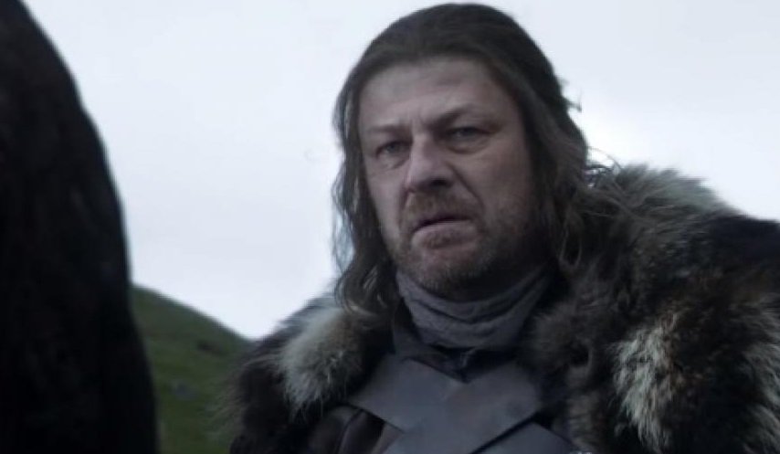 Ned Stark com cabelo preso e vestido com casaco de pele