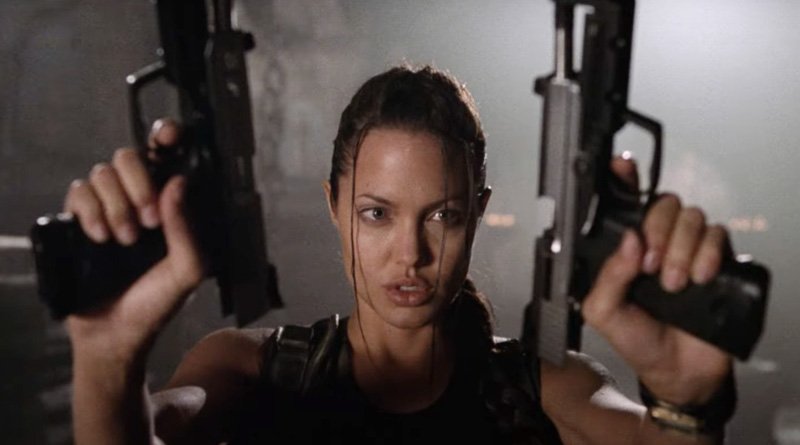 Angelina interpretando a personagem Lara Croft segurando duas armas nas mãos