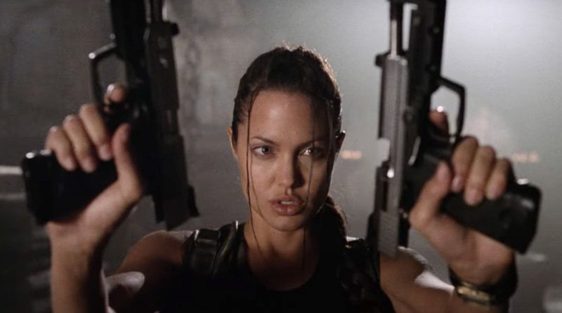 Reprodução / Paramount Pictures Angelina interpretando a personagem Lara Croft segurando duas armas nas mãos