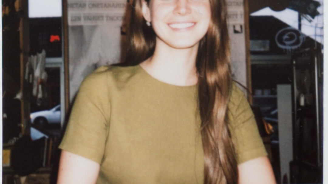 Lana Del Rey sorrindo e de braços cruzados.