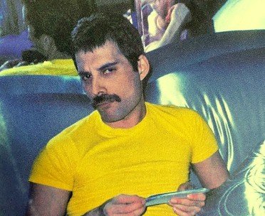 Freddie Mercury de camiseta amarela e olhando para a câmera
