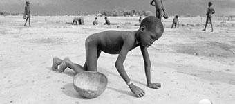 Criança extremamente magra, sem roupas, rastejando em areia.