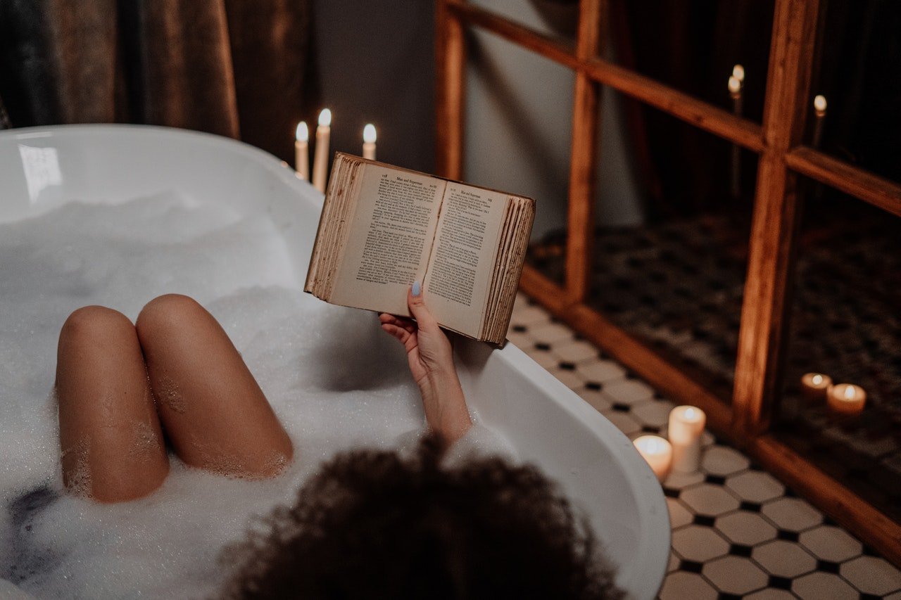 Mulher negra dentro de uma banheira enquanto lê livro.