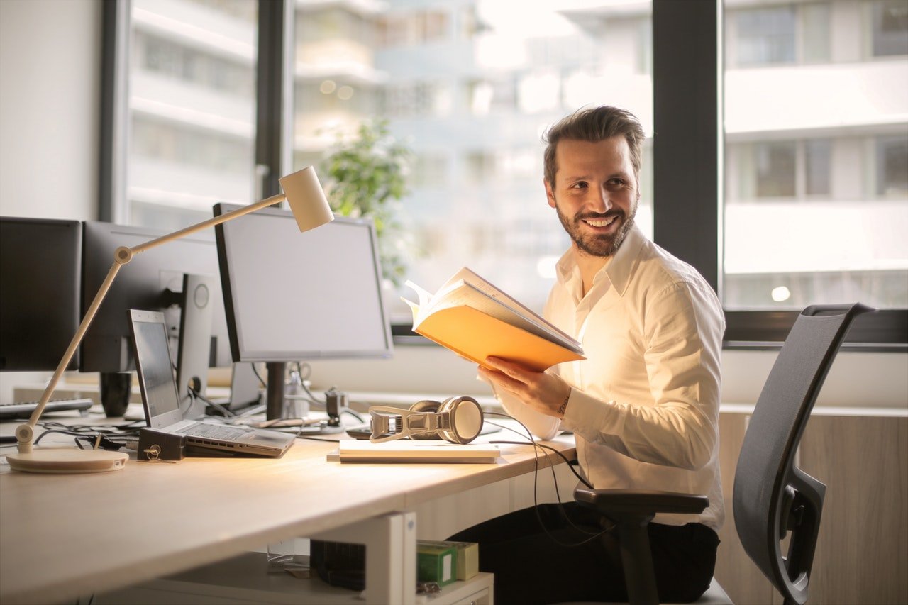 Homem em escritório sorri enquanto segura um caderno