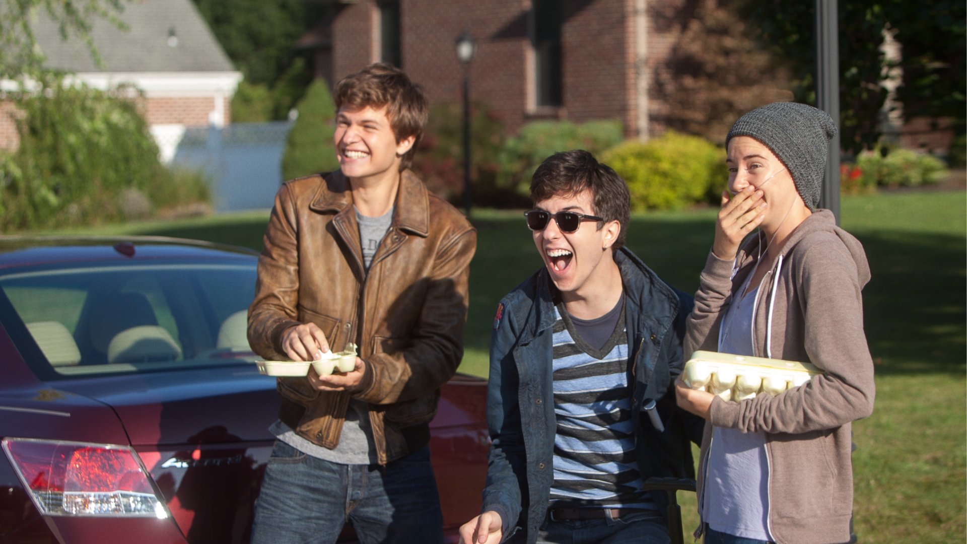 Da esquerda para a direita Hazel, Isaac e Gus na rua com caixas de ovos nas mãos