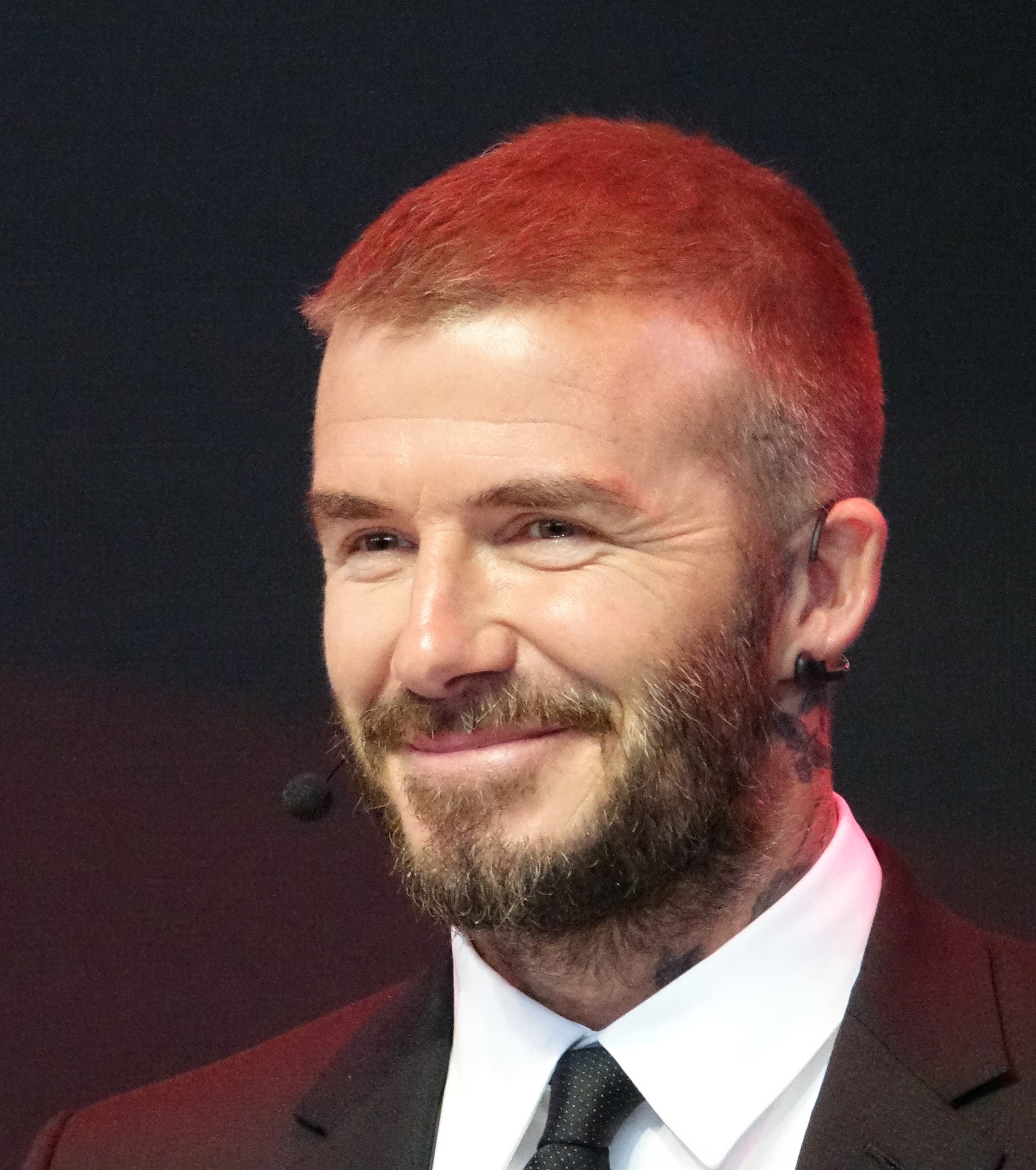 David Beckham usando roupas sociais e um microfone.