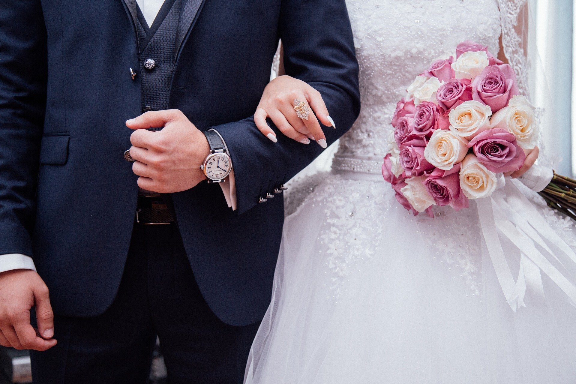 Homem vestido de terno e mulher com vestido de casamento, segurando buquê