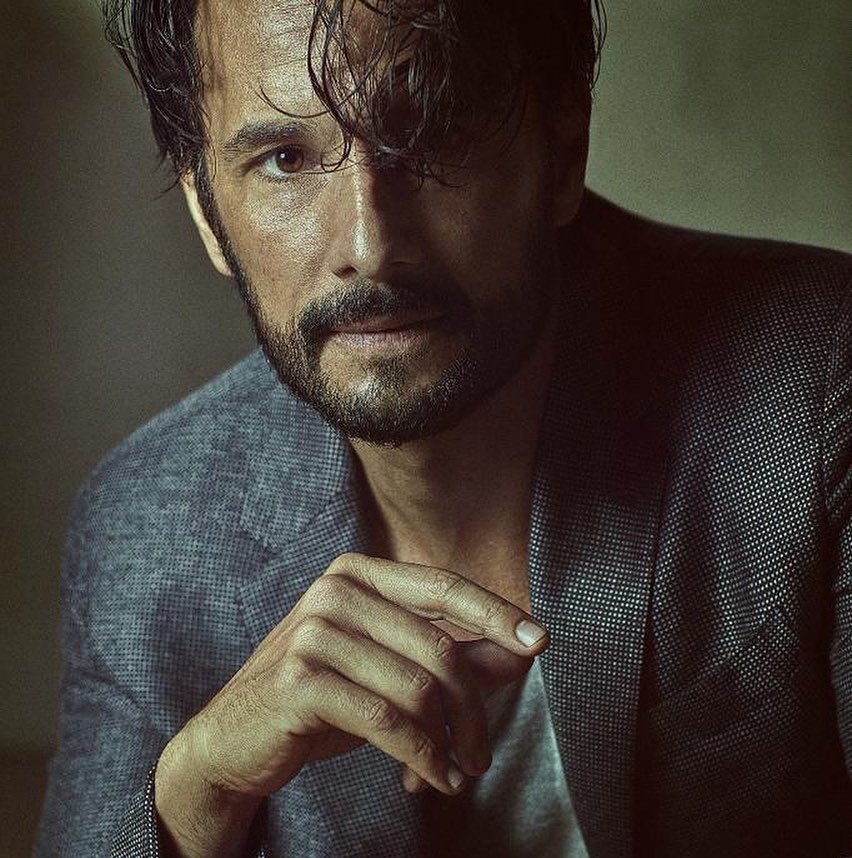 Reprodução/Instagram Rodrigo Santoro em sessão de fotos, com o cabelo levemente caído no rosto, e a mão solta em frente ao peito.