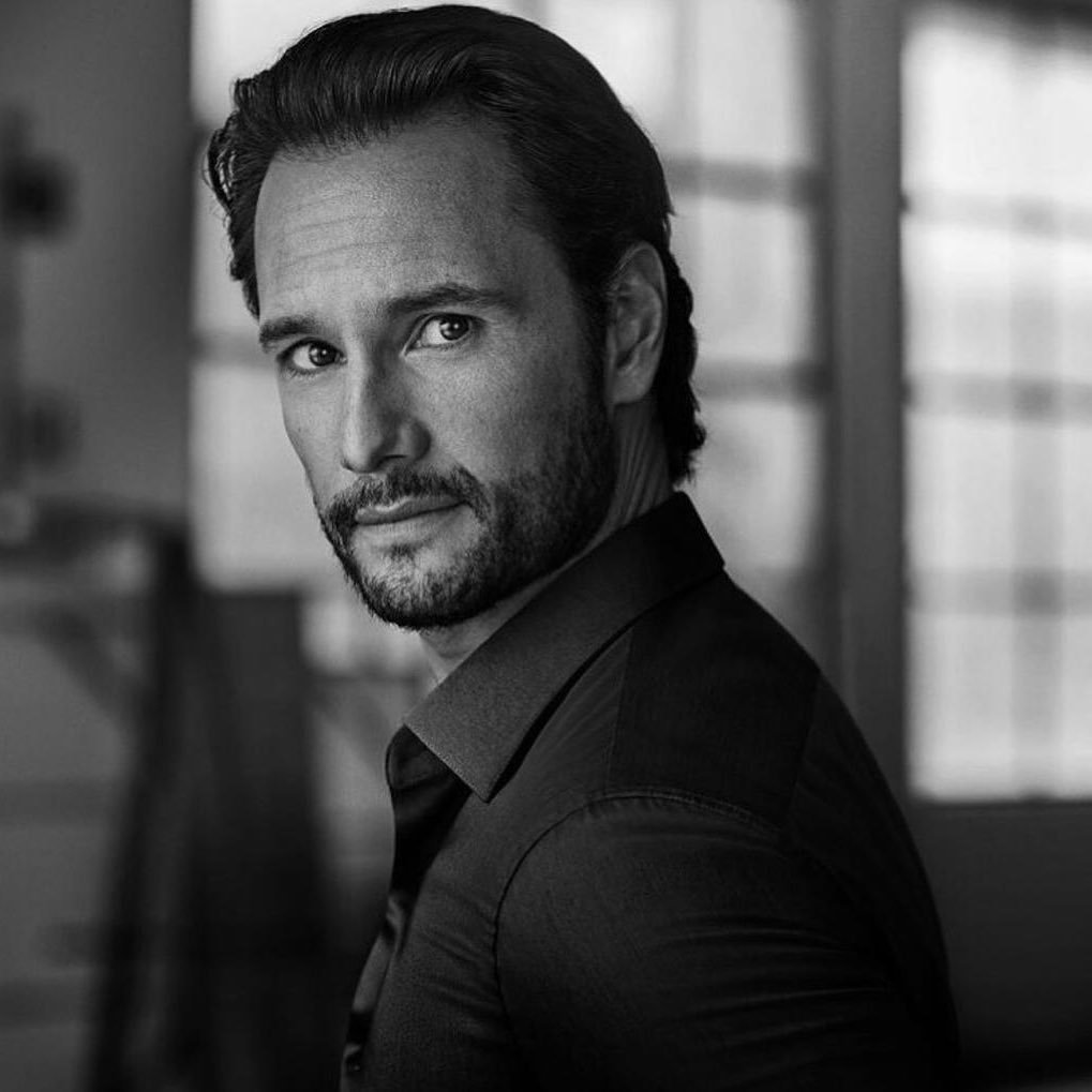 Rodrigo Santoro em sessão de fotos, usando terno e olhando para o lado.