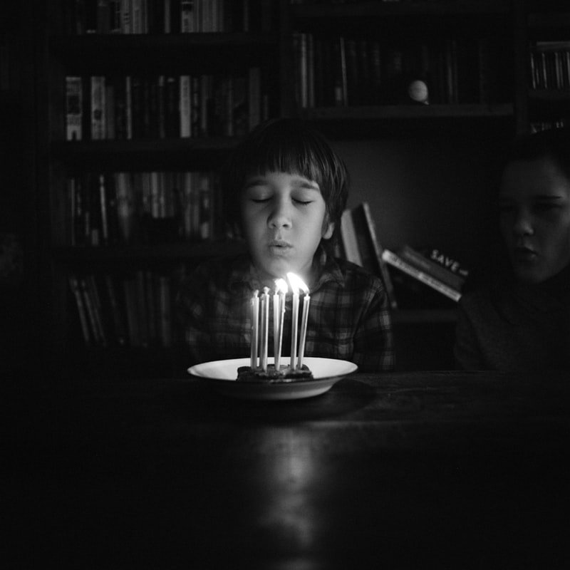 Unsplash/Annie Spratt Criança assoprando pedaço de bolo com velas de aniversário.
