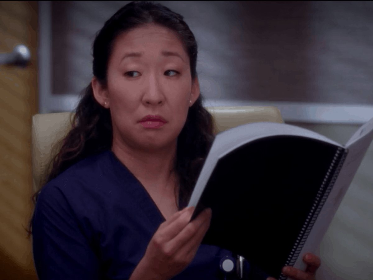 Cristina Yang segurando caderno, olhando para o lado.