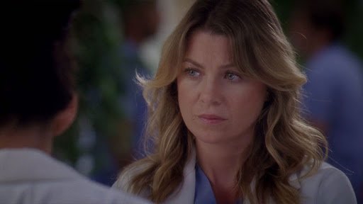 Meredith Grey usando vestimentas médicas e com expressão séria.