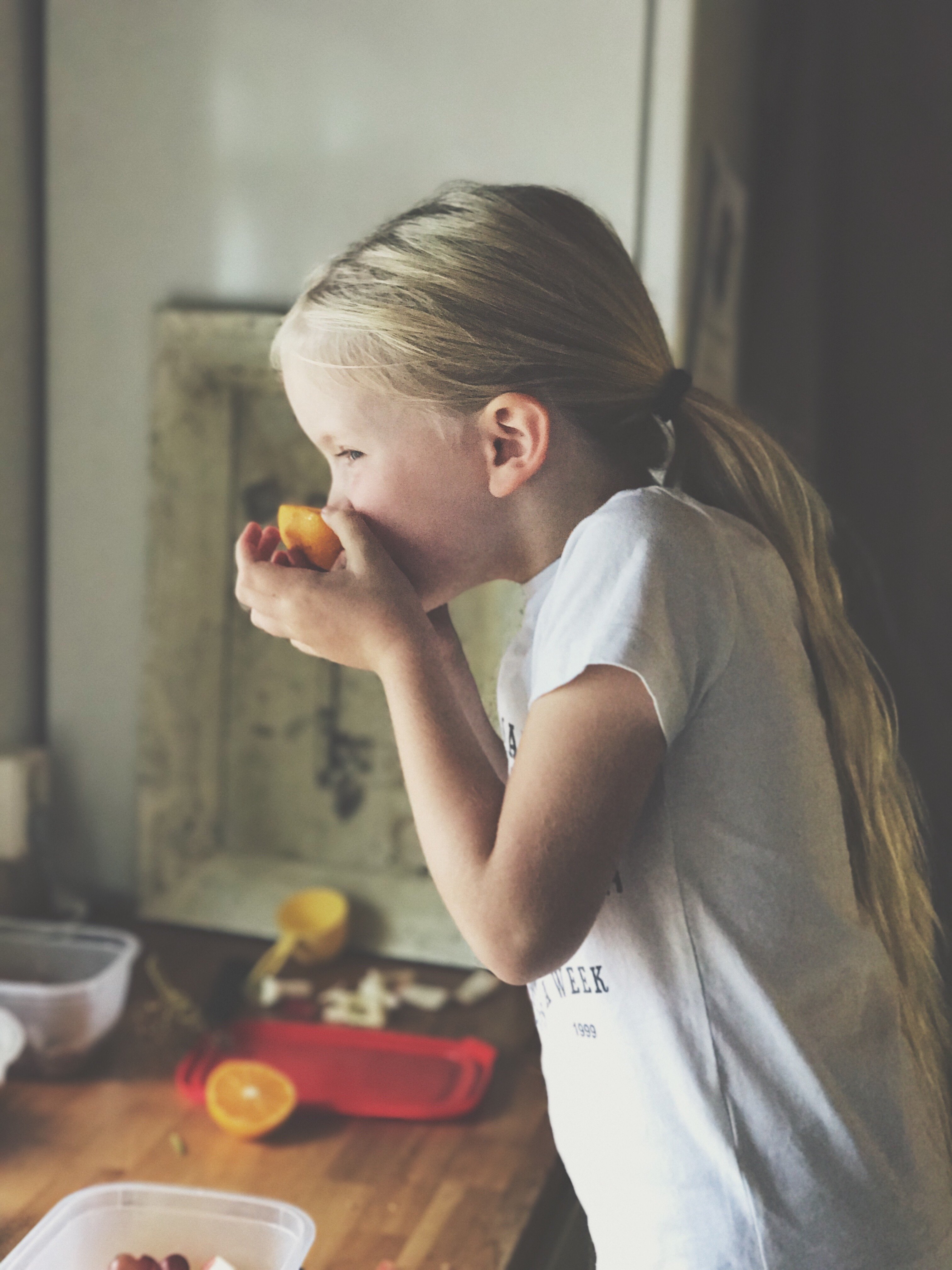 Criança comendo uma laranja na cozinha