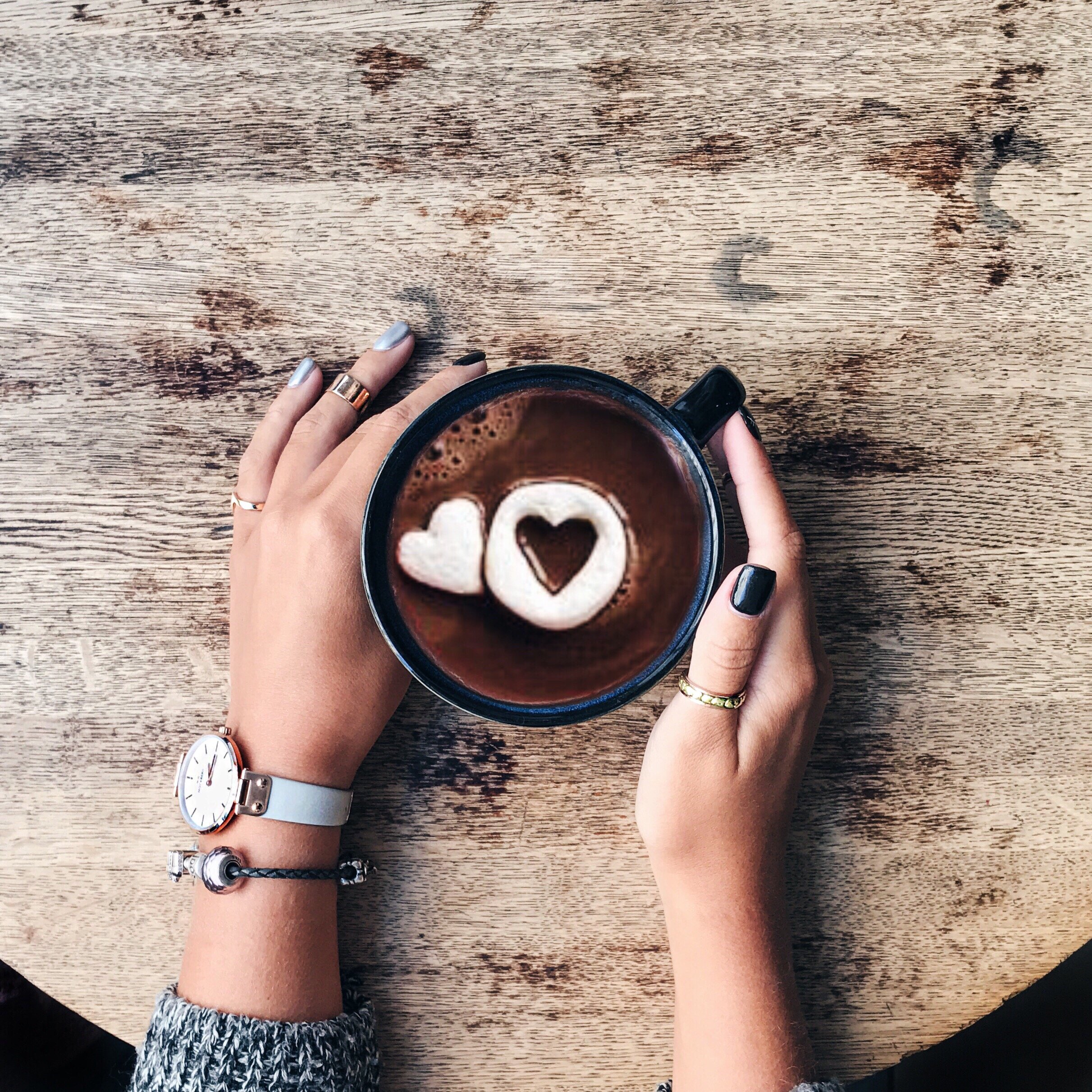 Mãos de mulher segurando xícara de chocolate quente que tem chocolates em formato de coração