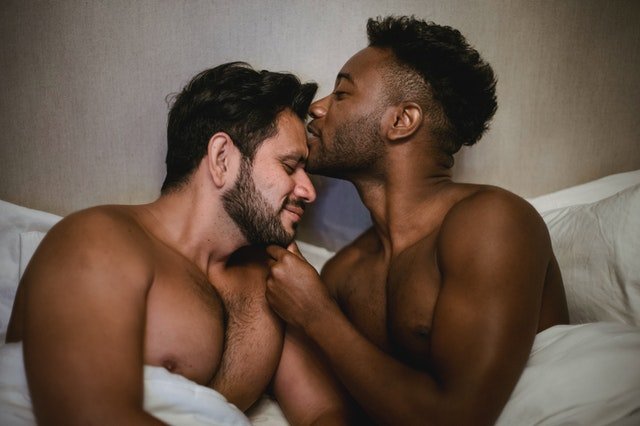 Casal de homens deitados na cama, com um beijando a testa do outro