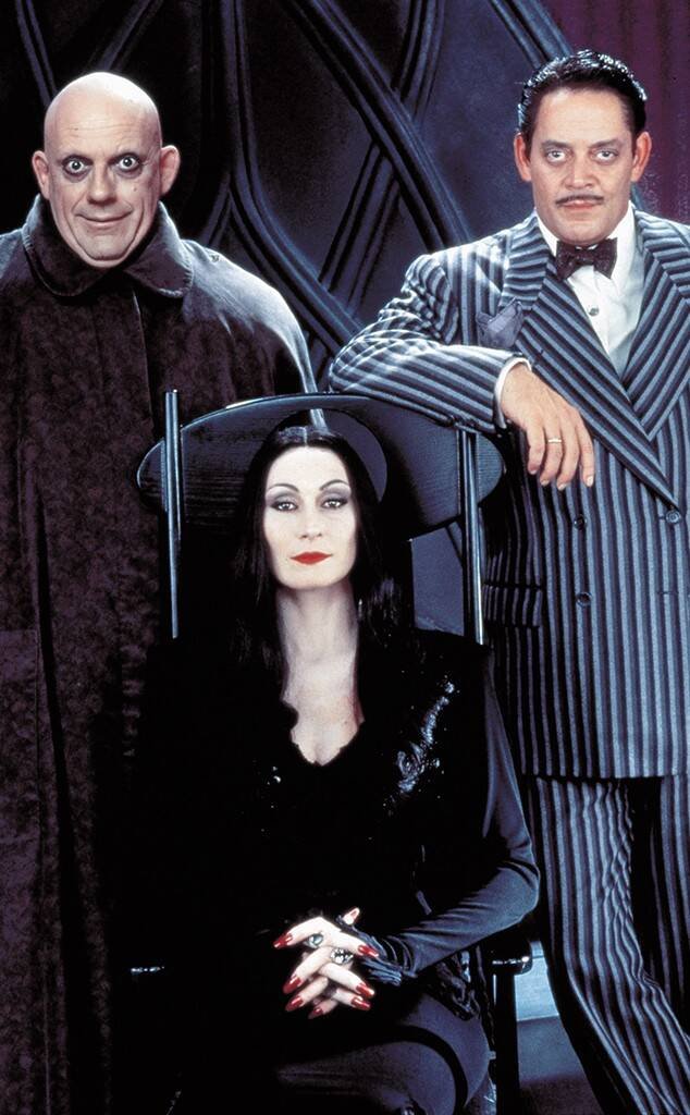 Sentada entre Raul Júlia, intérprete de Gomez Addams, e Christopher Lloyd, intérprete de Fester Addams, está Anjelica Huston como Mortícia.