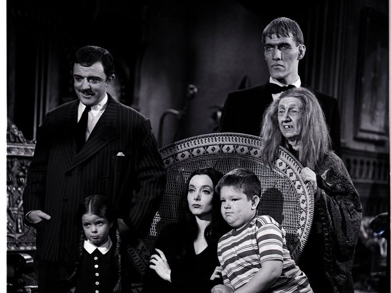 Elenco da Família Addams, década de 1960, reunida em sala de estar.