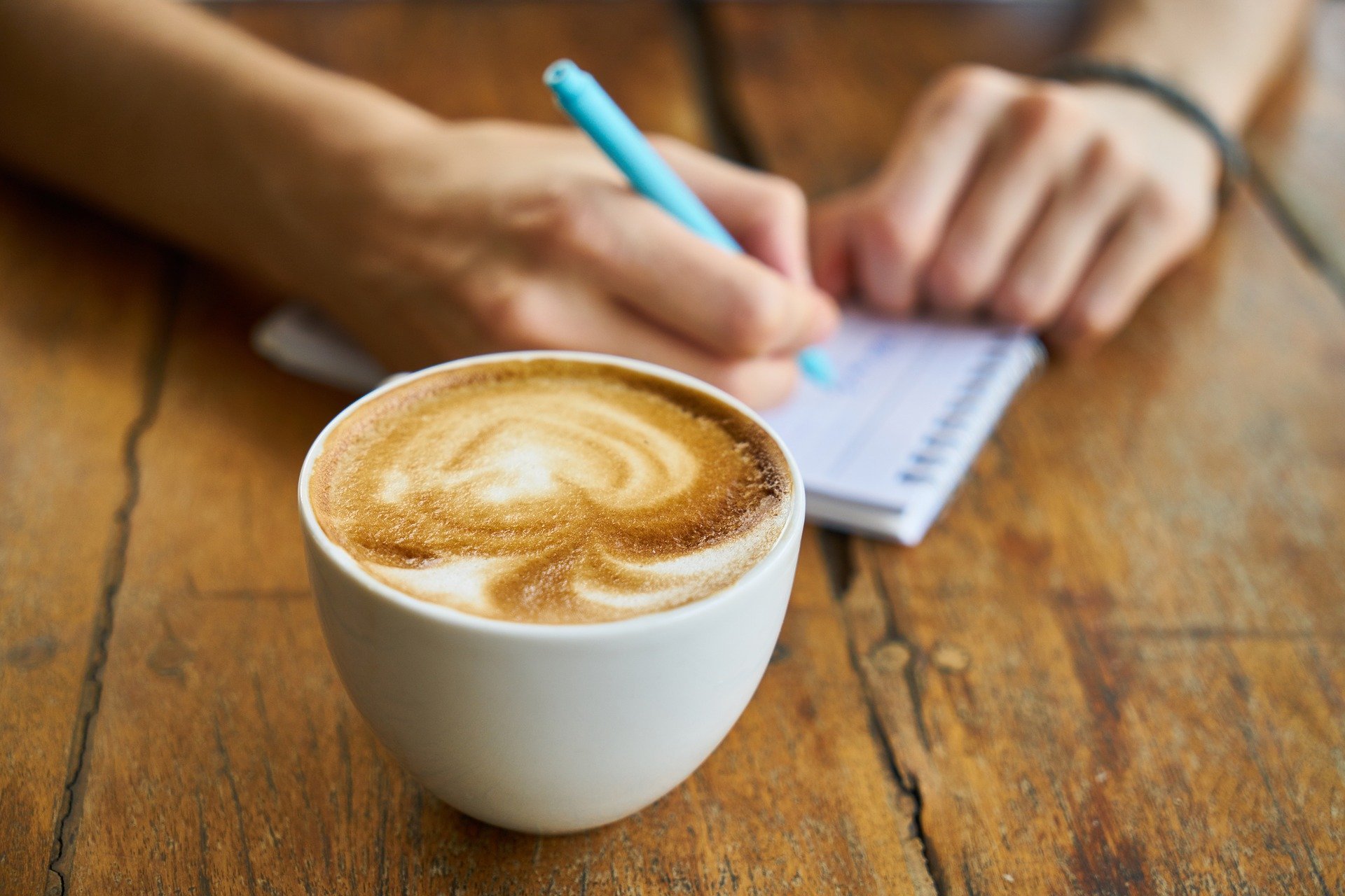Mulher fazendo uma anotação em uma agendinha ao lado de uma xícara de café