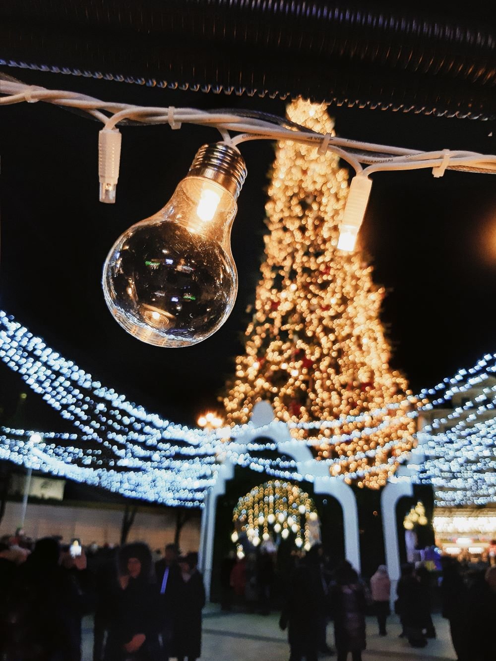 Lâmpada acesa próxima a uma árvore de natal iluminada e outras decorações de Natal.