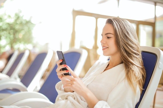 Pexels/Andrea Piacquadio Mulher deitada em cadeira de praia e mexendo no celular