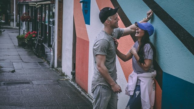 Homem apoia uma mão na parede, na frente de uma mulher