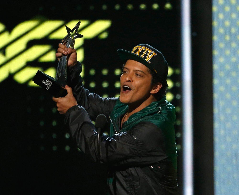 Bruno Mars recebendo prêmio BET, segurando o troféu para o alto e dando seu discurso.