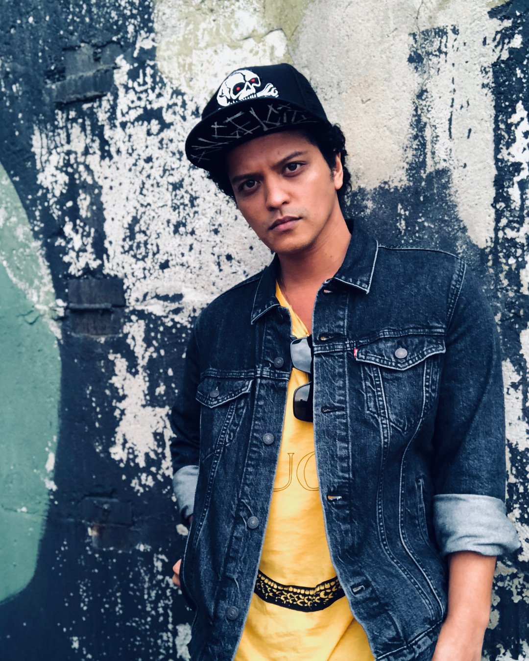 Bruno Mars posando para foto em frente de muro com grafite.