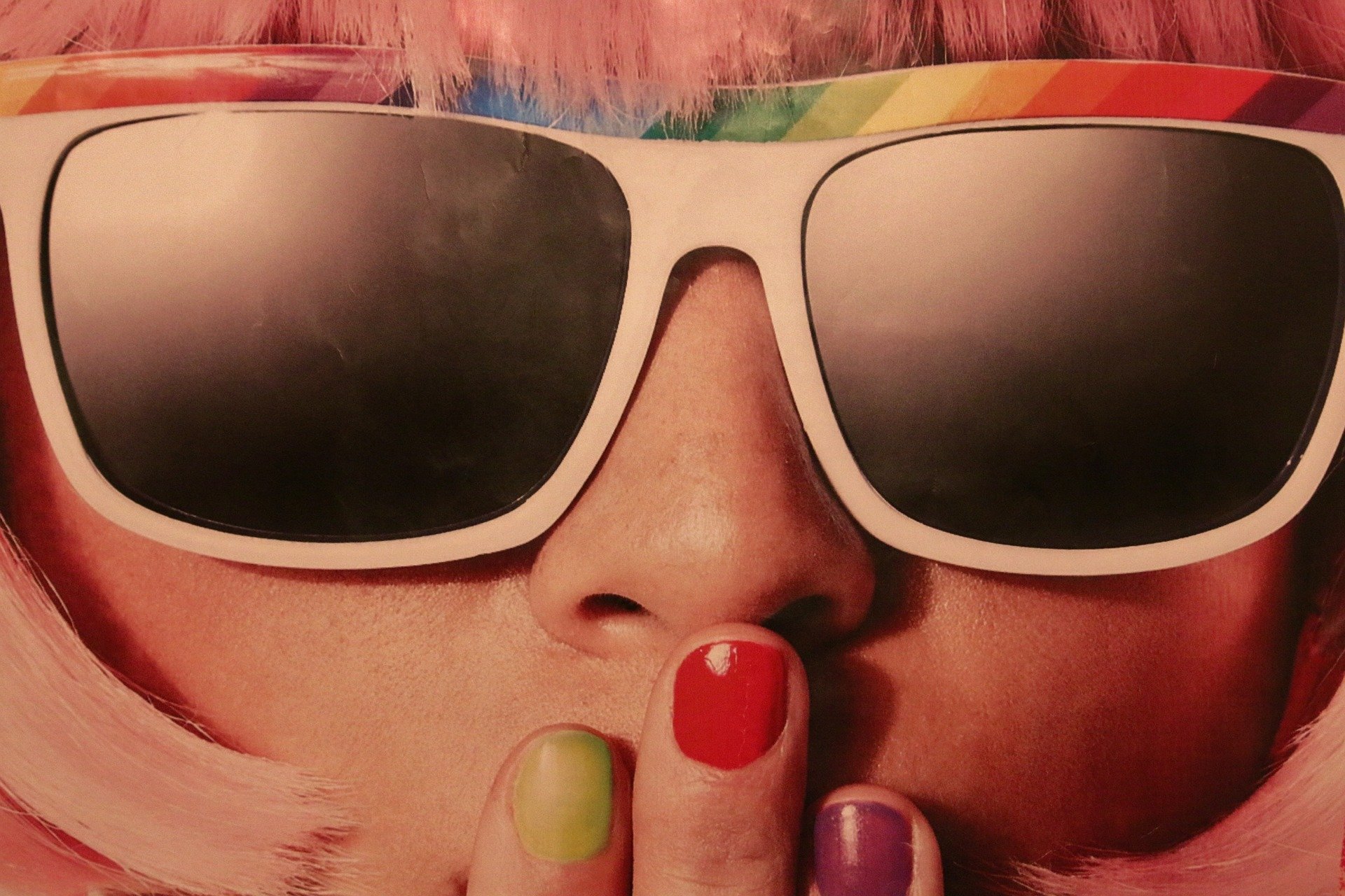 Pessoa vista de perto com óculos de sol e mão na boca com esmalte colorido