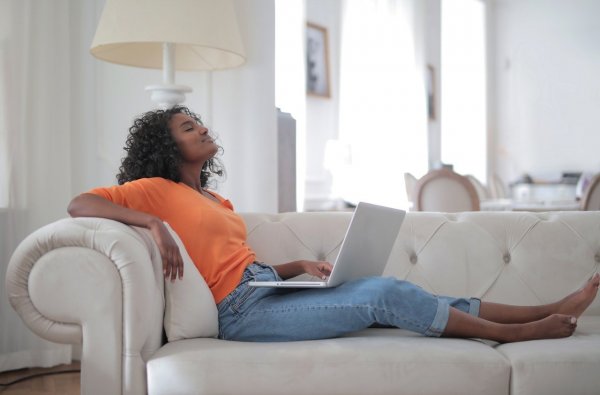 Pexels/Andrea Piacquadio Mulher deitada em sofá, com um notebook no colo, a cabeça inclinada para trás e os olhos fechados.