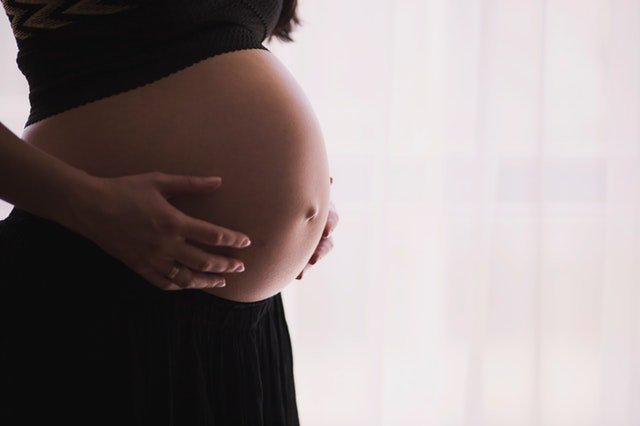 Mulher grávida, usando um top que deixa sua barriga exposta, com as duas mãos encostadas nas laterais da mesma.