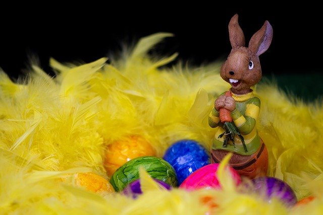 Estátua de coelho em madeira, com ovos coloridos em sua frente, dentro de um ninho feito com plumas amarelas.