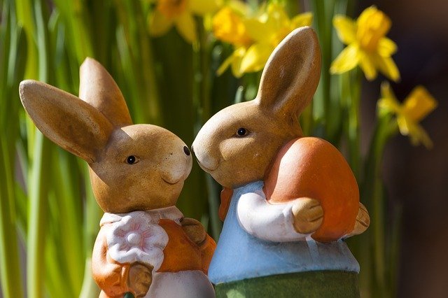 Estátuas de coelhos em cerâmica. Uma mostra uma fêmea segurando uma flor, olhando para a outra, de um macho segurando um ovo.