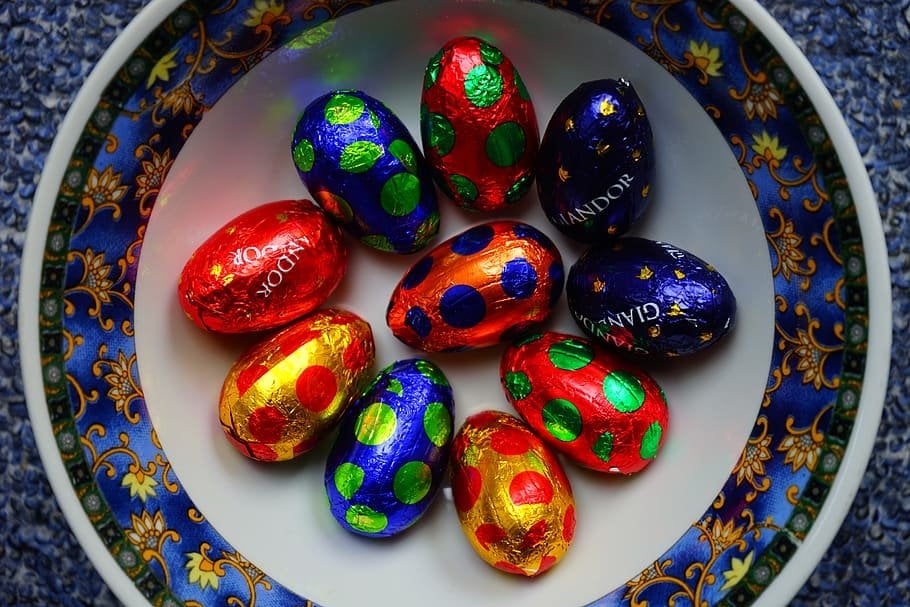 Pequenos ovos de chocolate embalados em papel metálico de várias cores, dentro de um prato de cerâmica.