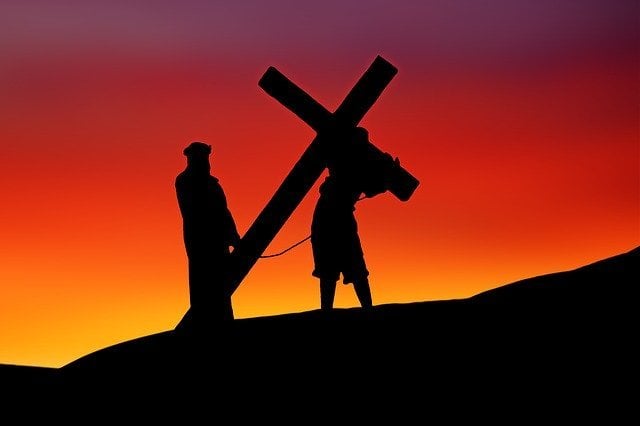 Silhueta de atores simulando Jesus carregando a cruz.
