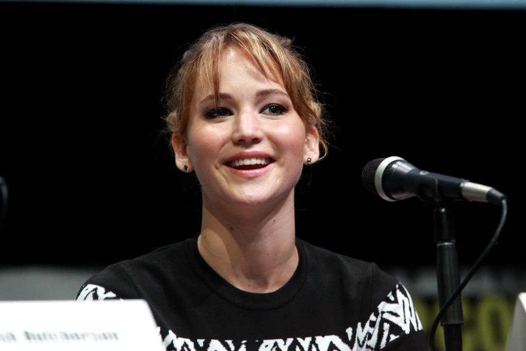 Jennifer Lawrence sentada com um microfone na frente rindo e olhando para frente