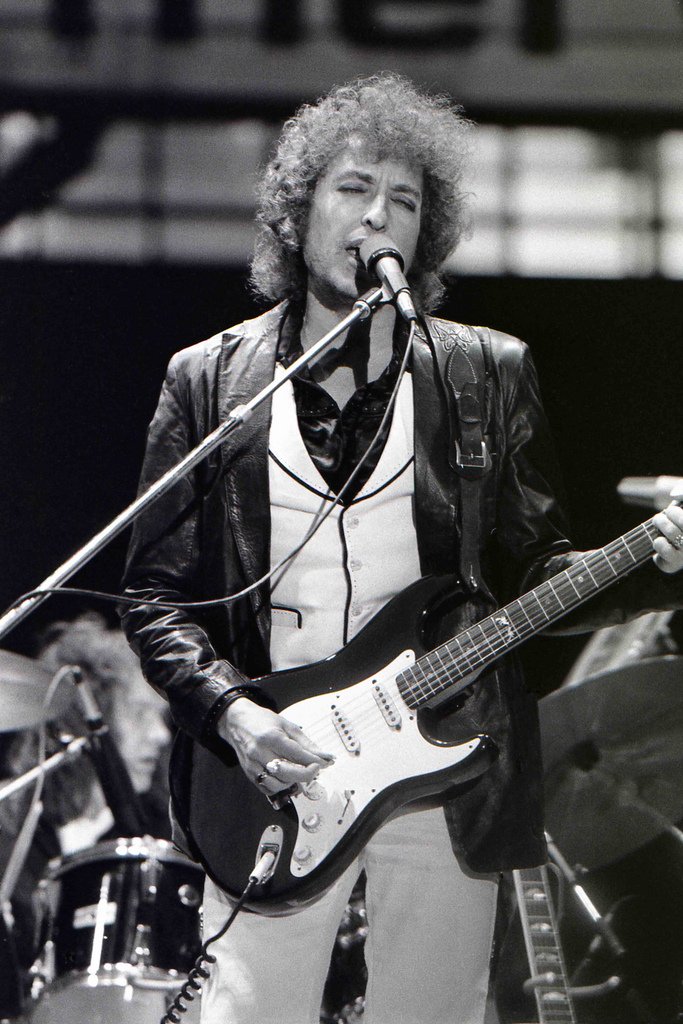 Bob Dylan em apresentação de show com guitarra na mão cantando