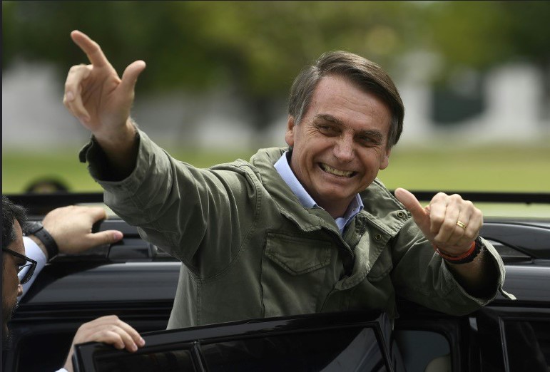 Bolsonaro entrando em seu carro, fazendo sinal de arma com as mãos.